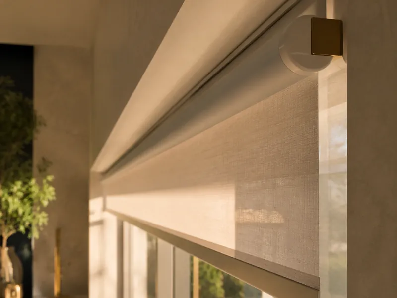 Detail of a motorized roller shade tube and bracket at the top of a tall window